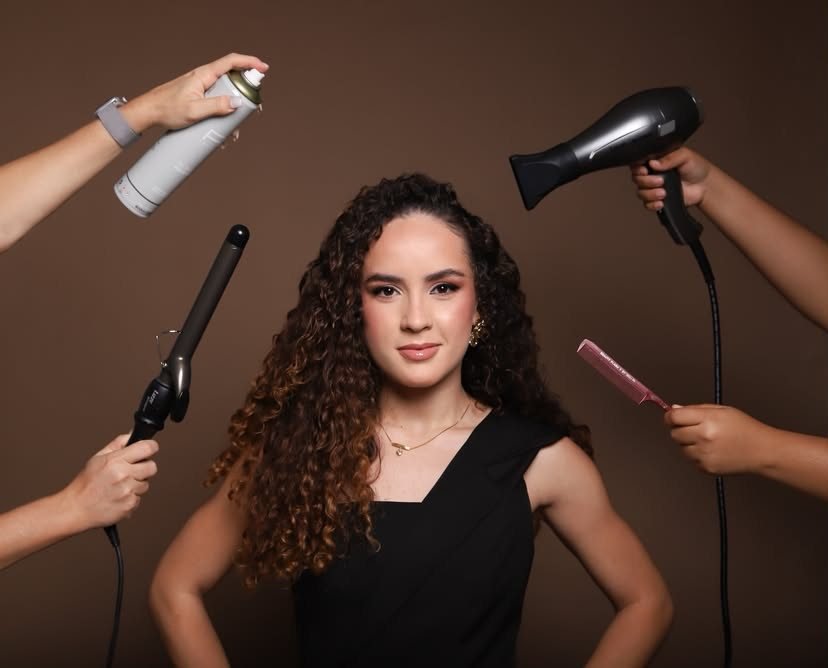 Mãos segurando secador, babyliss, spray e pente ao redor de Larissa Lima